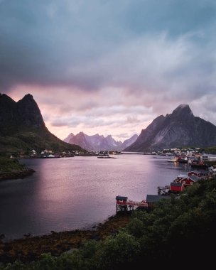 Çarpıcı dağlar alacakaranlıktaki sakin sulara zarif bir şekilde yansıyor, güzel ve bereketli doğayla çevrili. Reine, Lofoten Adaları, Norveç.
