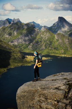 Bir yürüyüşçü, Norveç 'te nefes kesici bir fiyorda ve karlı dağlara bakarken görkemli bir uçurumda duruyor..