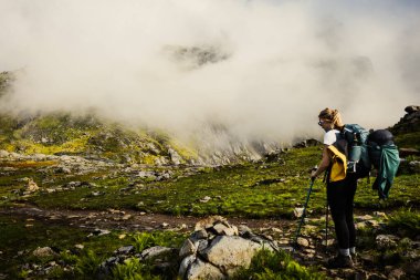Yalnız bir yürüyüşçü, yoğun sis ve yemyeşil ile kaplı güzel bir dağ yolunda zarifçe yol alır. Lofoten, Norveç.