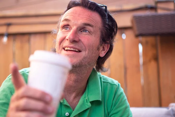 Man in a green golf shirt enjoying a coffee  on a patio in the summer time