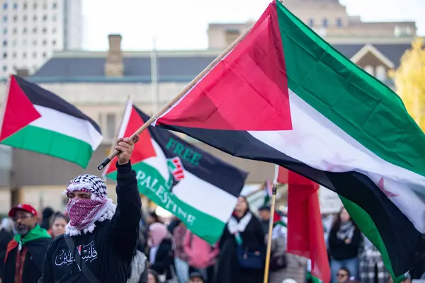 stock image Man wearing a keffiyeh holds a Palestinian flag up  at a Palestinian Protest against the war in Gaza in Toronto Ontario Canada