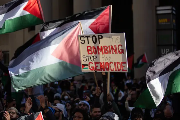 stock image Sign in the crowd sayin Stop the Bombing Stop the Genocide with Palestinian  flags in the background at a Protest at a Palestinian rally against the war in Gaza in Toronto Ontario Canada