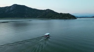 Skadar Gölü 'nde tekne. Skadar gölünde yüzen bir eğlence teknesi yolcuları dağın etrafından geçirir. Güneş çoktan dağların ardında kaybolmuştur..