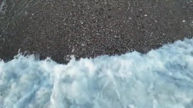Çakıl taşlı sahilde köpüklü deniz suyu