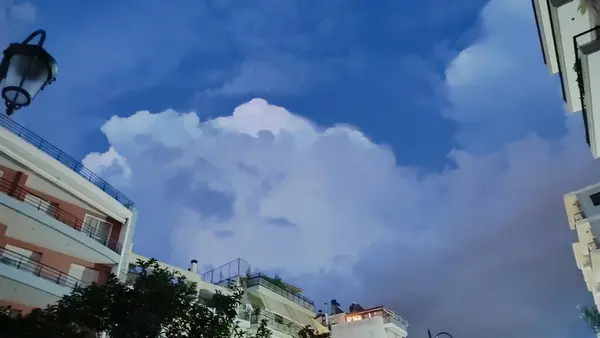 Uçsuz bucaksız, bulutlu gökyüzüne bakarken, binaların silueti, yukarıdaki kayan bulutlara karşı ön planda belirgin bir şekilde beliriyor.
