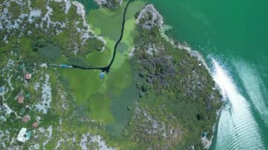 Parıldayan, kristal berrak suyla çevrili canlı yeşil bir adayı gösteren çarpıcı bir hava görüntüsü.