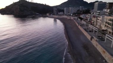 Güzel bir sahil manzarası sakin bir gün batımı görkemli dağlar ve yakınlardaki sakin suları gösteriyor.