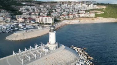 Huzurlu suların kıyısında duran görkemli bir deniz feneri. Arkasında yüksek dağlar var.