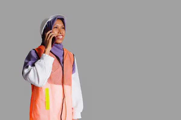 笑顔のイスラム教徒の女性労働者は 安全ヘルメットとベストを着て ホワイトバックで隔離された電話を持っています 労働日のコンセプト — ストック写真