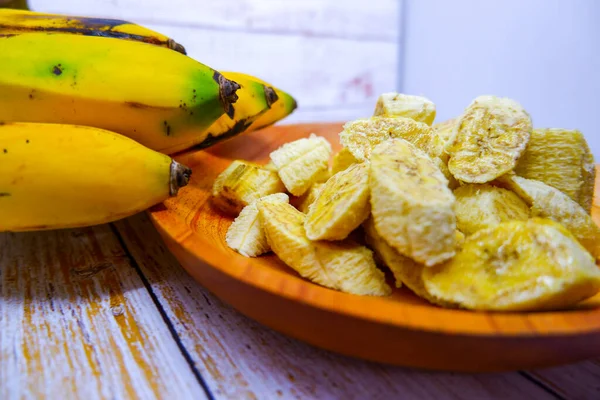 A banch of bananas and a sliced banana in a wood plate over a table.