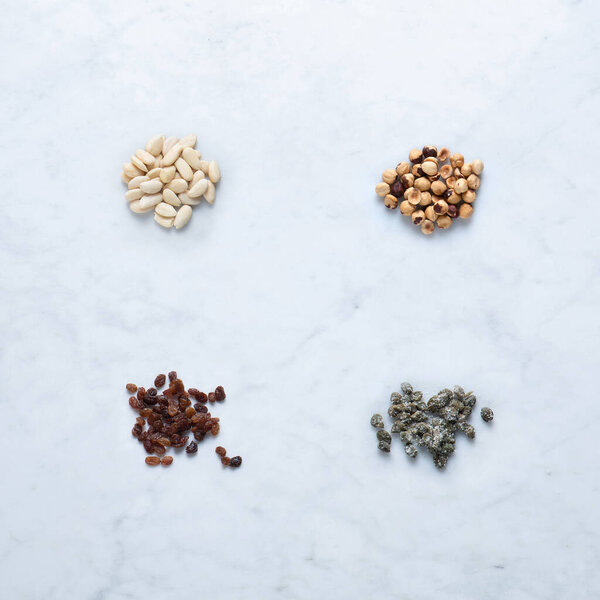 Ingredients from Italy for Seasoning, Isolated on Marble Background  Heaps of Almond and Hazelnut Peeled Dried Fruit, Raisins, Salted Capers in Bunch  Close-Up Macro, Top View, from Above