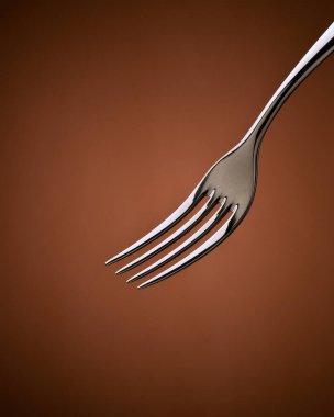 Paslanmaz çelik çatalın yakın planında sıcak kahverengi bir arka plan, çatal dolusu makarna.