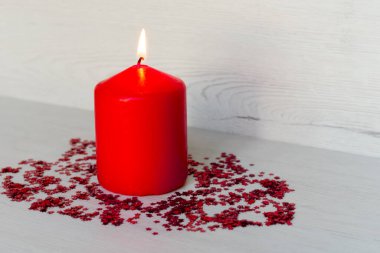 Kırmızı mum, etrafında küçük kırmızı yıldızlar ve açık arkaplan.