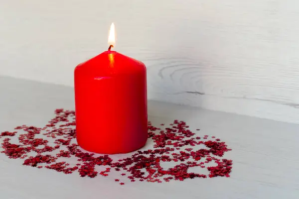 Kırmızı mum, etrafında küçük kırmızı yıldızlar ve açık arkaplan.