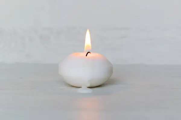 lit small white candle on a light wooden background