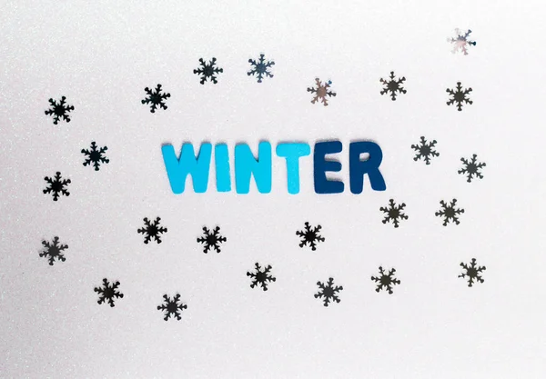 Açık arkaplanda kar taneleri olan mavi tonlarda kış kelimesinin olduğu renkli harfler.