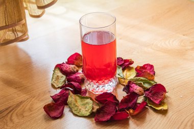 Bardakta kırmızı bir gül ve tahta bir masada bir fincan çay..