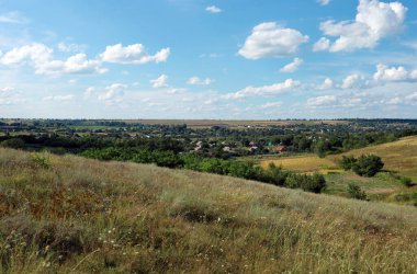 Uzakta köy evleri, bahçeleri ve tarlaları olan resimli tepeler. Ukrayna kırsal arazisi. Yazın kırsal bölgede..