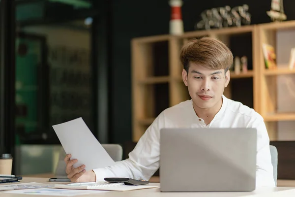 Asian young man doing accounting work using app and financial documents calculating salary of company employees and meeting online.