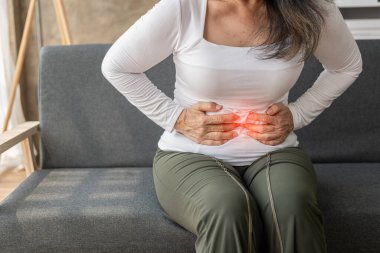 Asyalı son sınıf öğrencisi bir kadının evde koltukta otururken mide ağrısı çekmesi, gıda zehirlenmesi konsepti..