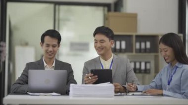 Bir grup Asyalı genç iş adamı iş planları ve dizüstü bilgisayarlardan finansal grafikler ve finansal grafikler sunarak ve açıklayarak ofiste toplantı ve beyin fırtınası yapıyorlar..