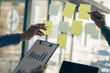 Toplantı odasındaki cama notlar, iş adamı eli işaret eden notlar ve notlar yazmak için not defteri ya da çeşitli post-it notları içeren toplantı konuları resimleri kapat