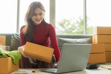 Küçük işletme kuruluşu, KME sahibi, dizüstü bilgisayarlı fatura kutuları üzerinde çalışan kadın girişimci ve müşterilere satılacak kutuları hazırlamak için çevrimiçi siparişleri kontrol eden.