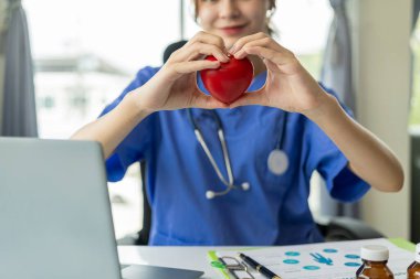 Kalp şeklinde kırmızı top tutan kadın doktor dizüstü bilgisayarda hastaya kardiyoloji, sağlık hizmetleri, sağlık hizmetleri kavramını açıklıyor.