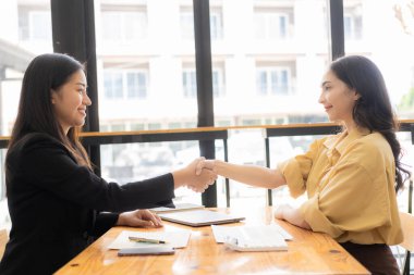 İki Asyalı iş kadını, ofiste takım çalışmasının önemi nedeniyle veri yığınını analiz ederken başarılı bir şekilde el sıkışıyor.