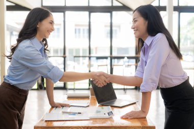 İki Asyalı iş kadını, ofiste takım çalışmasının önemi nedeniyle veri yığınını analiz ederken başarılı bir şekilde el sıkışıyor.
