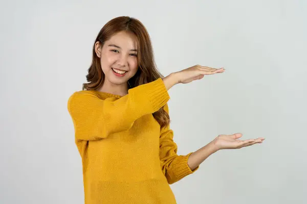 兴奋的亚洲女人在孤立的背景下举手表决 促销广告的概念快乐的少女穿着黄色衬衫站在白色房间里 — 图库照片