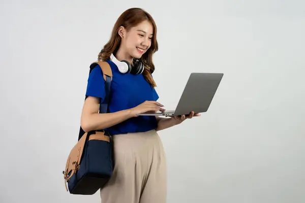 バックパックスタンドとラップトップを保持している幸せな若いアジアの女性学生 白い背景で隔離されたラップトップコンピュータで作業している青いTシャツの女性 オンライン教育の概念 — ストック写真