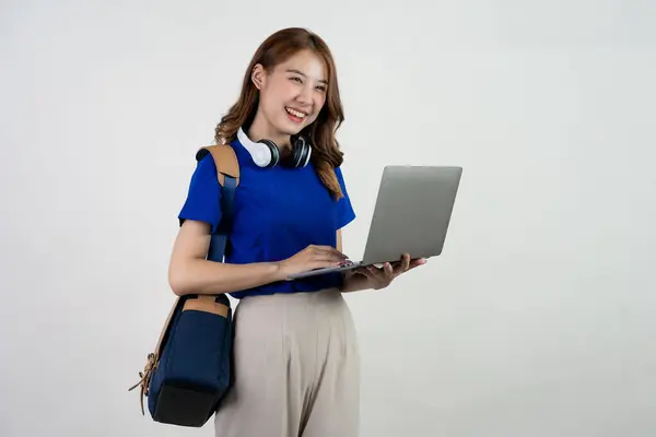 バックパックスタンドとラップトップを保持している幸せな若いアジアの女性学生 白い背景で隔離されたラップトップコンピュータで作業している青いTシャツの女性 オンライン教育の概念 — ストック写真