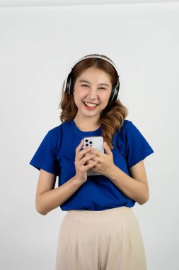 Akıllı telefon uygulamasından müzik çalan mutlu Asyalı genç kız beyaz arka planda müzik dinlerken mutlu bir gülümseme, teknoloji konsepti.