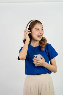 Akıllı telefon uygulamasından müzik çalan mutlu Asyalı genç kız beyaz arka planda müzik dinlerken mutlu bir gülümseme, teknoloji konsepti.