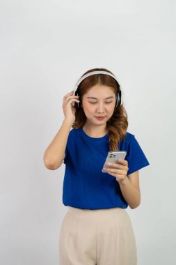 Akıllı telefon uygulamasından müzik çalan mutlu Asyalı genç kız beyaz arka planda müzik dinlerken mutlu bir gülümseme, teknoloji konsepti.