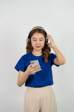 Akıllı telefon uygulamasından müzik çalan mutlu Asyalı genç kız beyaz arka planda müzik dinlerken mutlu bir gülümseme, teknoloji konsepti.