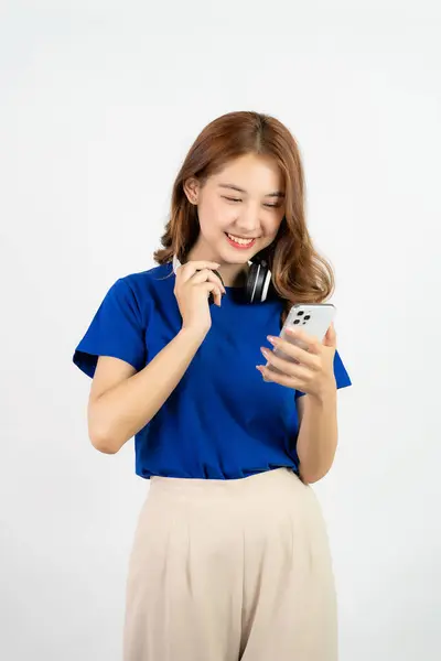 かなり幸せなアジアの十代の少女は スマートフォンアプリケーションから音楽を再生する携帯電話を使用して ホワイトバックグラウンド 技術コンセプトに対してストリーミングミュージックを聞いている間 幸せな笑顔 — ストック写真