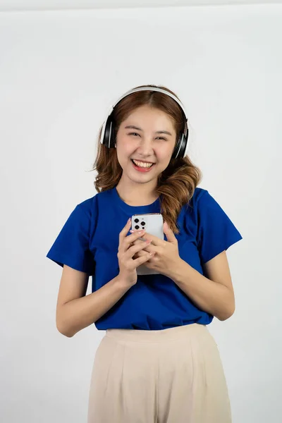 相当快乐的亚洲少女使用手机播放智能手机应用程序中的音乐 开心的微笑着在白底背景下听流媒体音乐 科技概念 — 图库照片