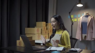 Asyalı kadın elbise stoklarını ve çevrimiçi perakende işini kontrol ediyor, İnternet satış sitesinde kıyafet satıyor, canlı yayınlar 4K video, moda tartışmaları ve çevrimiçi mağazada giysiler satıyor.