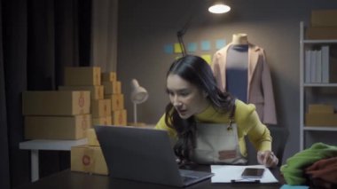 Asyalı kadın elbise stoklarını ve çevrimiçi perakende işini kontrol ediyor, İnternet satış sitesinde kıyafet satıyor, canlı yayınlar 4K video, moda tartışmaları ve çevrimiçi mağazada giysiler satıyor.