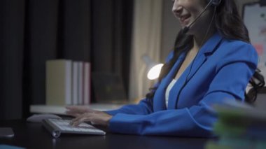 İş yerinde kulaklık takan genç Asyalı bir kadın, internet toplantısı ev bilgisayarı kullanan genç bir kadın çağrı merkezi operatörü, kulaklık takıyor ve müşteri desteği ile gülümsüyor.