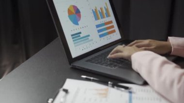 Çekici Asyalı iş kadını dizüstü bilgisayarla çalışıyor ve finansal belgeleri kontrol ediyor ve şirket muhasebe hesaplarını ofisdeki masada analiz ediyor.