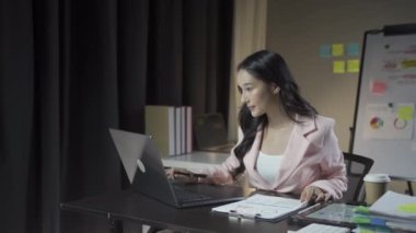 Çekici Asyalı iş kadını dizüstü bilgisayarla çalışıyor ve finansal belgeleri kontrol ediyor ve şirket muhasebe hesaplarını ofisdeki masada analiz ediyor.
