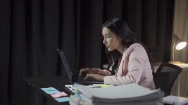 Çekici Asyalı iş kadını dizüstü bilgisayarla çalışıyor ve finansal belgeleri kontrol ediyor ve şirket muhasebe hesaplarını ofisdeki masada analiz ediyor.