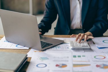 Muhasebeci fatura yatırım grafiğini analiz eder ve belge muhasebe memuru, banka danışmanı ve yakın çekim fotoğrafındaki denetçi üzerine hesap makinesi düğmesine basar