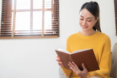 Güzel genç Asyalı kadın evdeki oturma odasında dinleniyor. Tatilde mutlu bir duyguyla kitap oku..