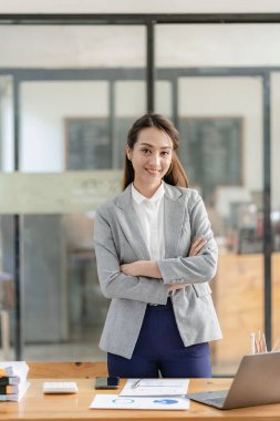 Masada oturan Asyalı iş kadını kağıtları ve dizüstü bilgisayarla iş hesaplarını ve finansal planlama kavramlarını analiz ediyor..