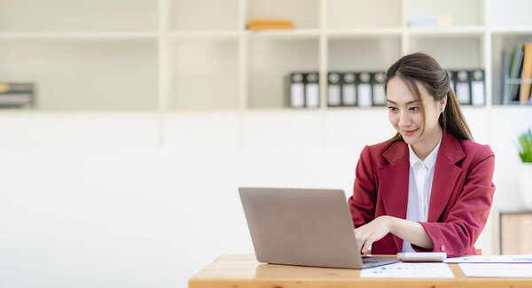 Asian businesswoman working with papers and laptop sitting at table in office, analyzing business accounting calculations and financial planning concepts.
