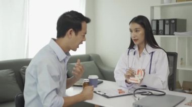 Beyaz laboratuvar önlüğü ve sınav eldivenleriyle gülümseyen güzel kadın dişçi, diş aletleri kullanıyor ve diş sağlığı kliniğinde diş modeli olan genç erkek hastayı muayene etmeye başlıyor..